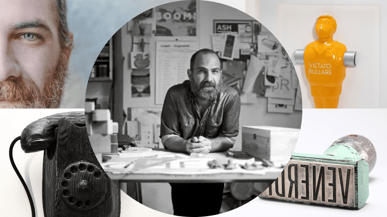 Johnny Hermann in posa nel suo studio, circondato dalle sue sculture in legno come un telefono vintage e figure umane stilizzate utilizzate come giocatori di calcio balilla